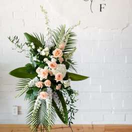 Peach roses and white flowers in a tall standing spray with palm leaves