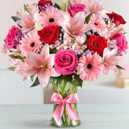 Pink and red mixed flower bouquet in a glass vase with a pink ribbon