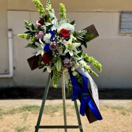 Standing floral wreath with white lilies, red roses, and blue ribbon on an easel