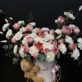 Pink and white roses with carnations in a white hatbox, with a teddy bear attached
