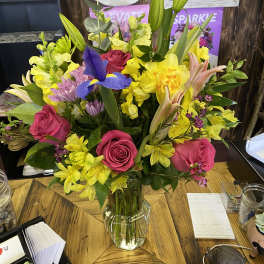 Mixed bouquet of pink roses, yellow daffodils, and purple iris in a glass vase