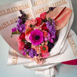 Pink and purple mixed bouquet wrapped in paper with "LOVE IS ETERNAL" text