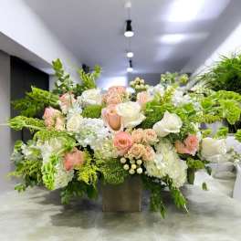 Large floral arrangement with white and blush roses in a square vase