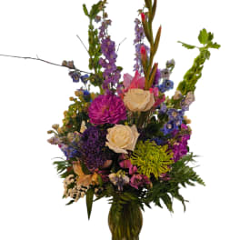 Tall mixed flower arrangement in a glass vase with purple, pink, and cream blooms