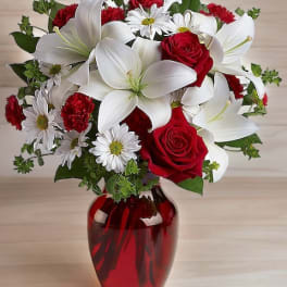 Bouquet of red roses, white lilies, and daisies in a red glass vase