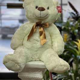 Cream teddy bear with a gold ribbon sitting on a pedestal