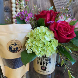 Mug arrangement with red roses and green hydrangea beside a kraft bag of coffee beans