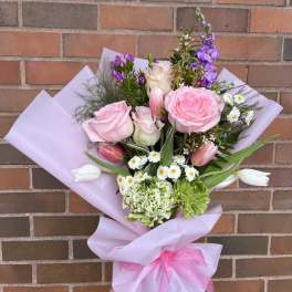 Bouquet of pink roses, tulips, and purple flowers wrapped in lavender paper