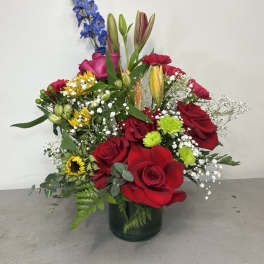 Mixed bouquet of red roses, lilies, and blue delphinium in a glass vase