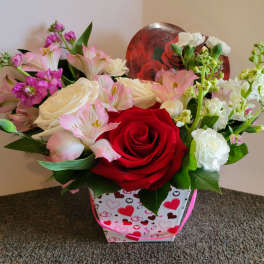 Mixed pink, white, and red flower arrangement in a heart-patterned gift bag