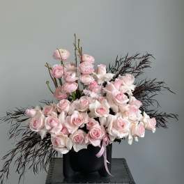 Pink roses and ranunculus in a black vase with dark feathery accents