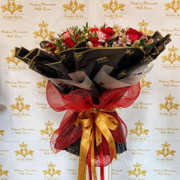 Large bouquet of red and pink roses wrapped in black paper with a red and gold ribbon