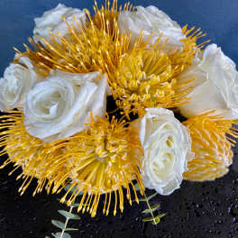 Low arrangement of white roses and yellow pincushion protea on a black round base