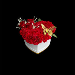 Red carnations and roses in a white heart-shaped box with a butterfly accent