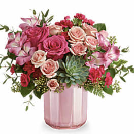 Pink and peach roses in a pink glass vase with greenery