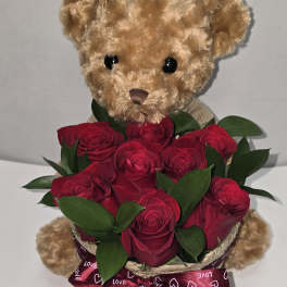 Teddy bear holding a bouquet of red roses with a heart ribbon