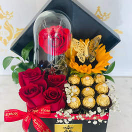 Red roses and chocolates arranged in a black gift box with a clear dome.