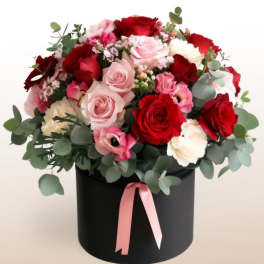 Bouquet of red and pink roses in a black hat box with a pink ribbon