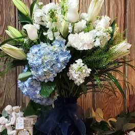 Large bouquet of white lilies, white blooms, and blue hydrangeas in a dark vase