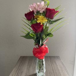 Tall bouquet of red roses and pink flowers in a glass vase with a red bow