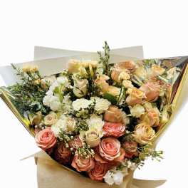 Bouquet of peach and cream roses with white flowers wrapped in gold and kraft paper