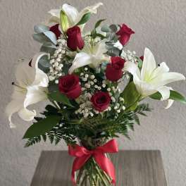 Bouquet of red roses and white lilies in a glass vase with a red ribbon