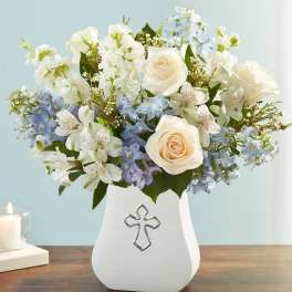 White and pale blue flower arrangement in a white vase with a cross emblem