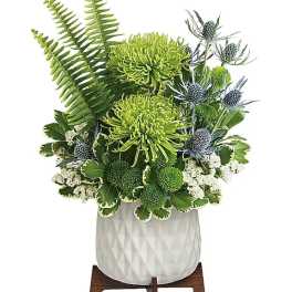 Green floral arrangement in a white textured vase on a wooden stand