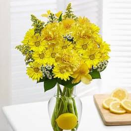 Yellow flower bouquet in a clear glass vase with a lemon inside