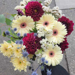 Handheld bouquet of cream and burgundy flowers with blue thistle accents