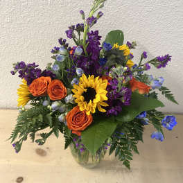 Mixed bouquet with sunflowers, orange roses, and purple flowers in a glass vase