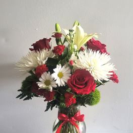 Bouquet of red roses, white lilies, and white daisies in a glass vase
