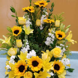 Yellow sunflowers, roses, and lilies arranged in a tall display