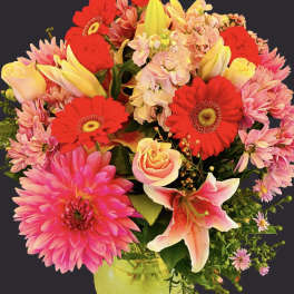 Bright mixed bouquet in a green vase with pink, red, and yellow blooms