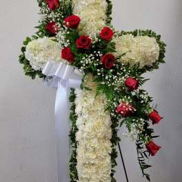 White floral cross with red roses and a white ribbon on a stand