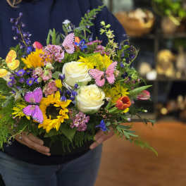 Colorful mixed flower arrangement in a black container with butterfly picks