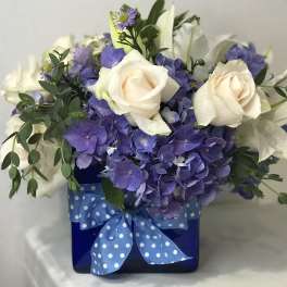 White roses and purple hydrangeas in a blue box with a polka-dot ribbon
