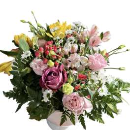 Mixed bouquet of pink, yellow, and white flowers in a white vase