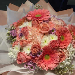 Bouquet of pink gerbera daisies, roses, and white chrysanthemums wrapped in paper