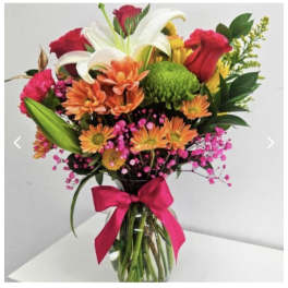 Mixed bouquet of lilies, roses, and daisies in a glass vase with a pink ribbon