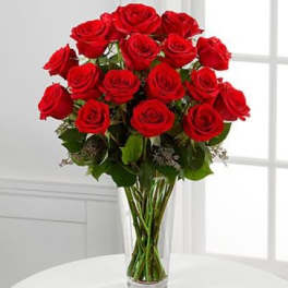 Tall clear vase filled with long-stemmed red roses.