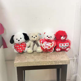 Four plush teddy bears holding heart pillows on a table