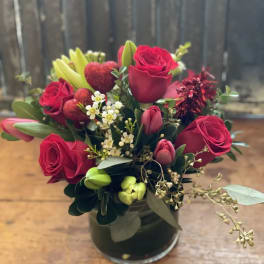 Red roses and tulips arranged in a glass vase with small white filler flowers