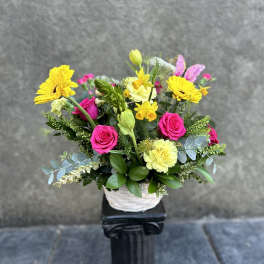 Bright mixed flower arrangement in a white basket with pink roses and yellow daisies