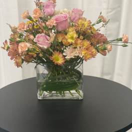 Pink roses and mixed blooms in a clear square vase