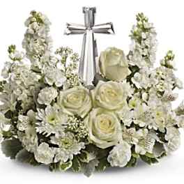 White floral arrangement with roses and stock around a silver cross