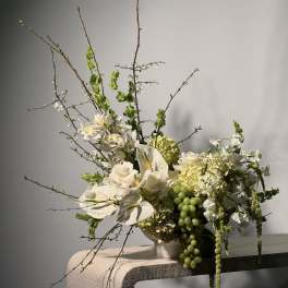 White floral arrangement with orchids, roses, and green grapes in a vase