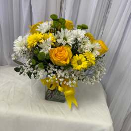Yellow roses and white daisies in a glass vase with a yellow ribbon