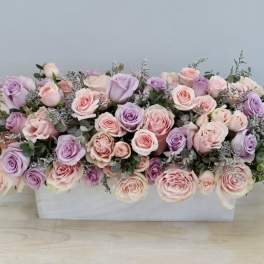 Low rectangular arrangement of pink and lavender roses in a white container