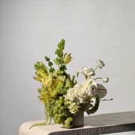 White and green floral arrangement in a vase with grapes and an apple